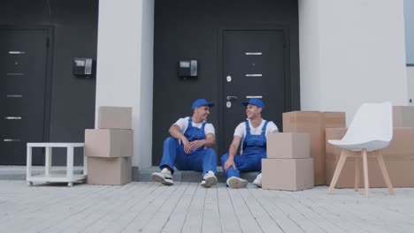 two removal company workers have a break while sitting on the step