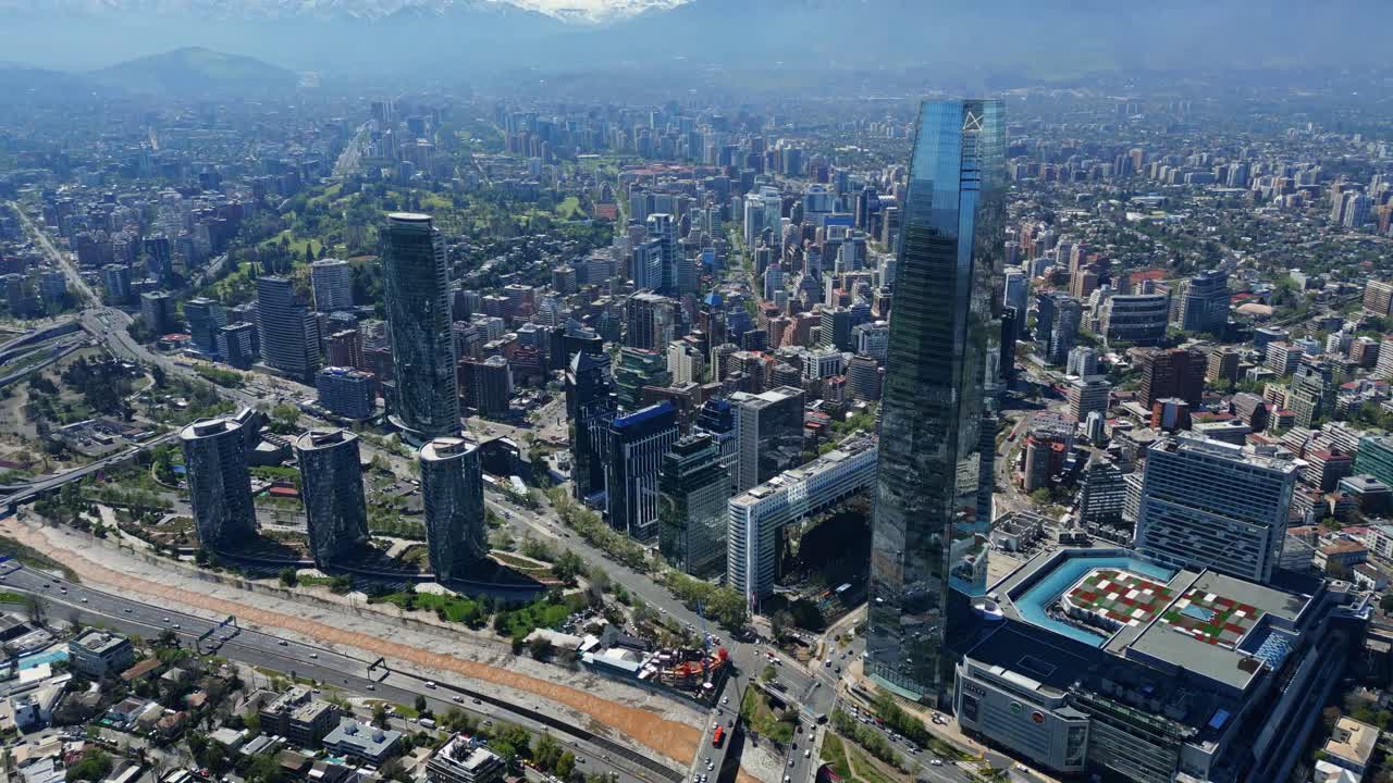 Ripresa aerea da drone in avvicinamento e panoramica sui grattacieli, le autostrade e i tetti del Costanera, con luce diurna nitida e le Ande all'orizzonte. Santiago, Cile