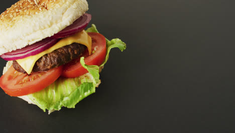 Vídeo-De-Hamburguesa-Con-Queso-Con-Ensalada-En-Pan-De-Hamburguesa,-Sobre-Fondo-Gris-Con-Espacio-Para-Copiar