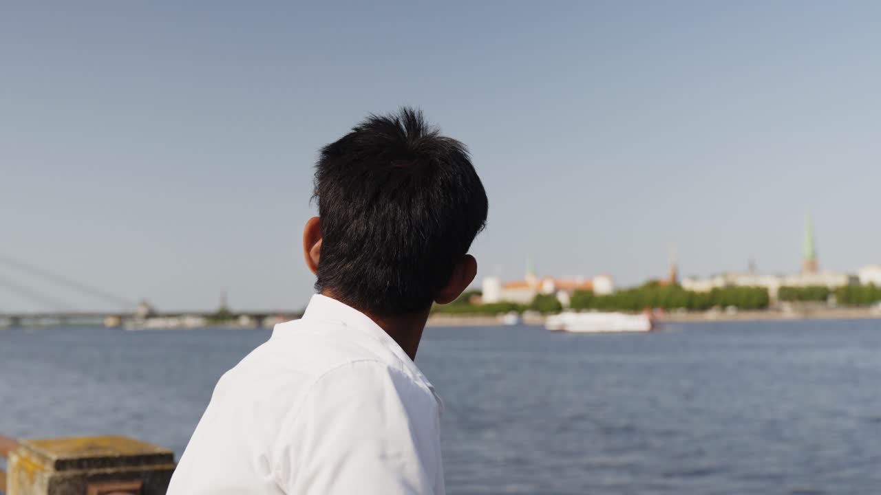 다리 위의 카메라를 향해 돌고 있는 흰 셔츠를 입은 젊은 갈색 피부의 남자의 클로즈업