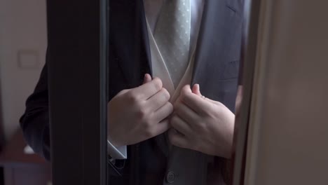 groom fixing his dark suit and white tie through a window before wedding ceremony