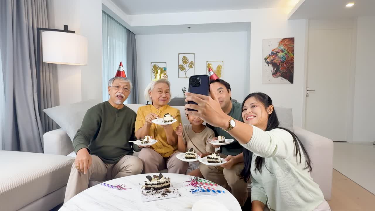 Four generations enjoy birthday cake, smiling for a selfie in a brightly lit living room