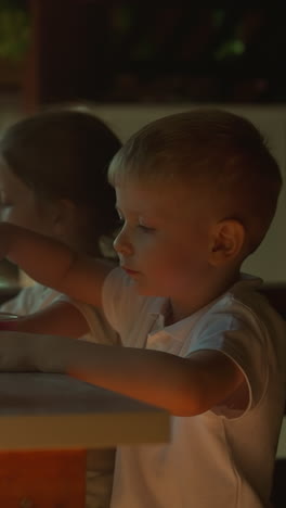 niño pequeño come helado sentado con su hermana y su madre en una cafetería en cámara lenta. familia feliz sabe postres fríos visitando un restaurante. almuerzo de verano