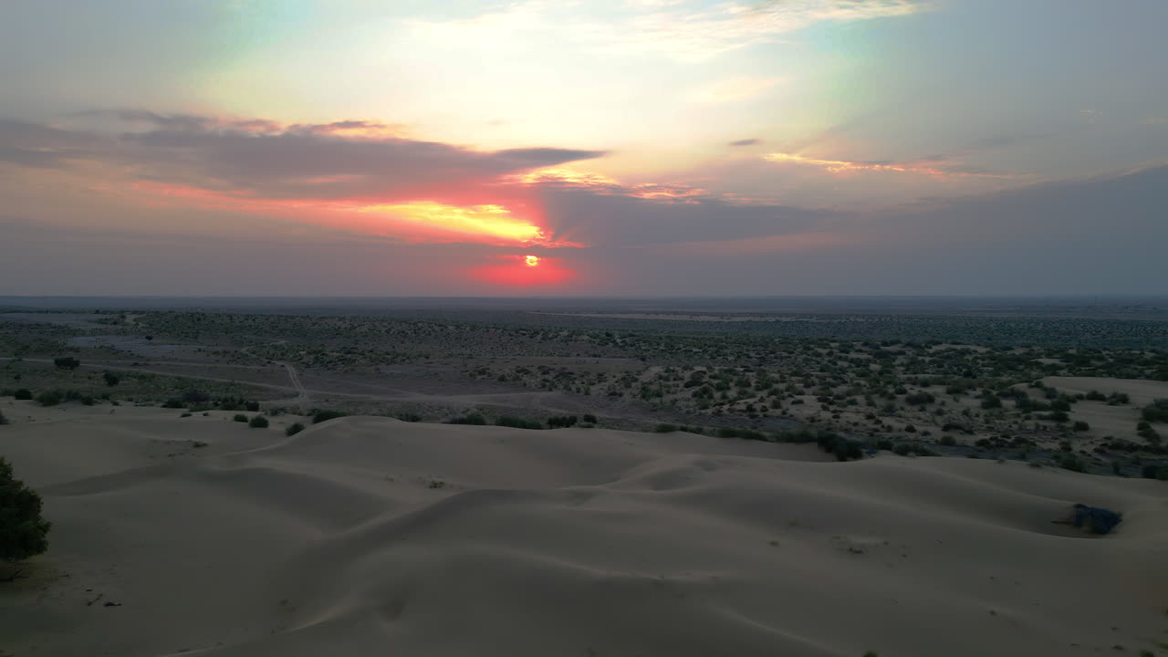 Endless expanse of golden dunes glows under a dramatic sunrise sky, painted in hues of orange, pink and purple, Scattered green bushes Jaisalmer Rajasthan India 4K Drone