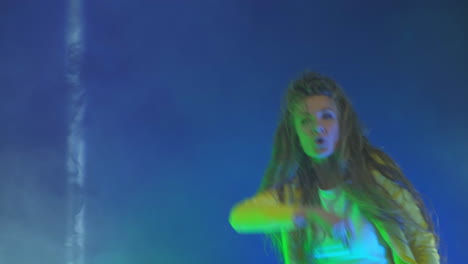 a funny woman in a yellow jacket jumps and dances energetically in the neon light and smoke