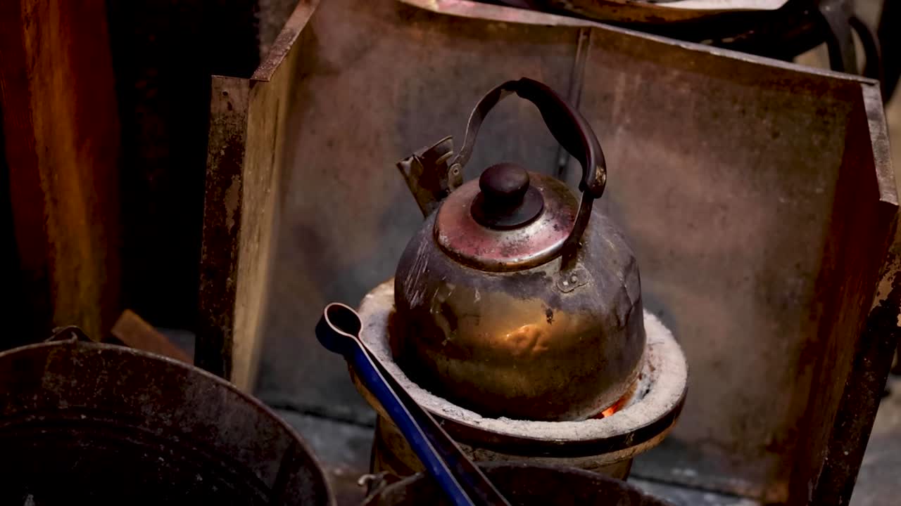 A rustic metal kettle sits atop a glowing charcoal stove for traditional water boiling