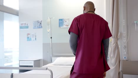 médico afroamericano preocupado sentado en la cama en una habitación de hospital, cámara lenta