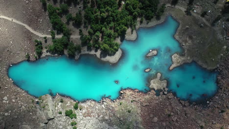 cinematic drone shot of turquoise colored water in the mountains at naltar valley in pakistan, downward angle aerial shot