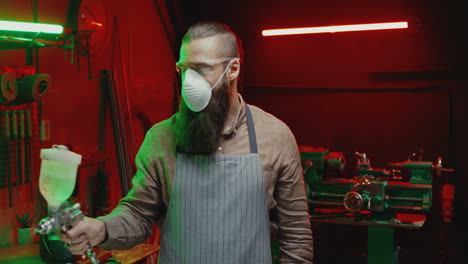 caucasian man in goggles, respiratory mask and apron working with pulverizator in workshop