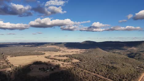 drone camera smoothly pans above timor rock, revealing expansive rural plains, forested hills, and dramatic clouds in afternoon sunlight near coonabarabran, australia