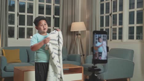 asian little boy shows trick with disappearing on mobile phone camera while recording on smartphone video content for social networks in cozy room