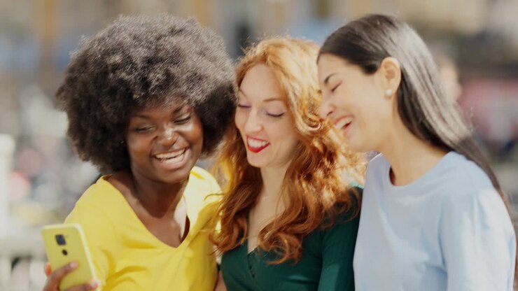 Three happy diverse friends laughing and interacting with a smartphone outdoors
