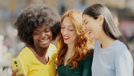 three happy diverse friends laughing and interacting with a smartphone outdoors