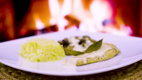 chuleta de pollo con crema y hongos, crema fresca, queso, arroz en un plato cuadrado con un fuego de leña en el fondo
