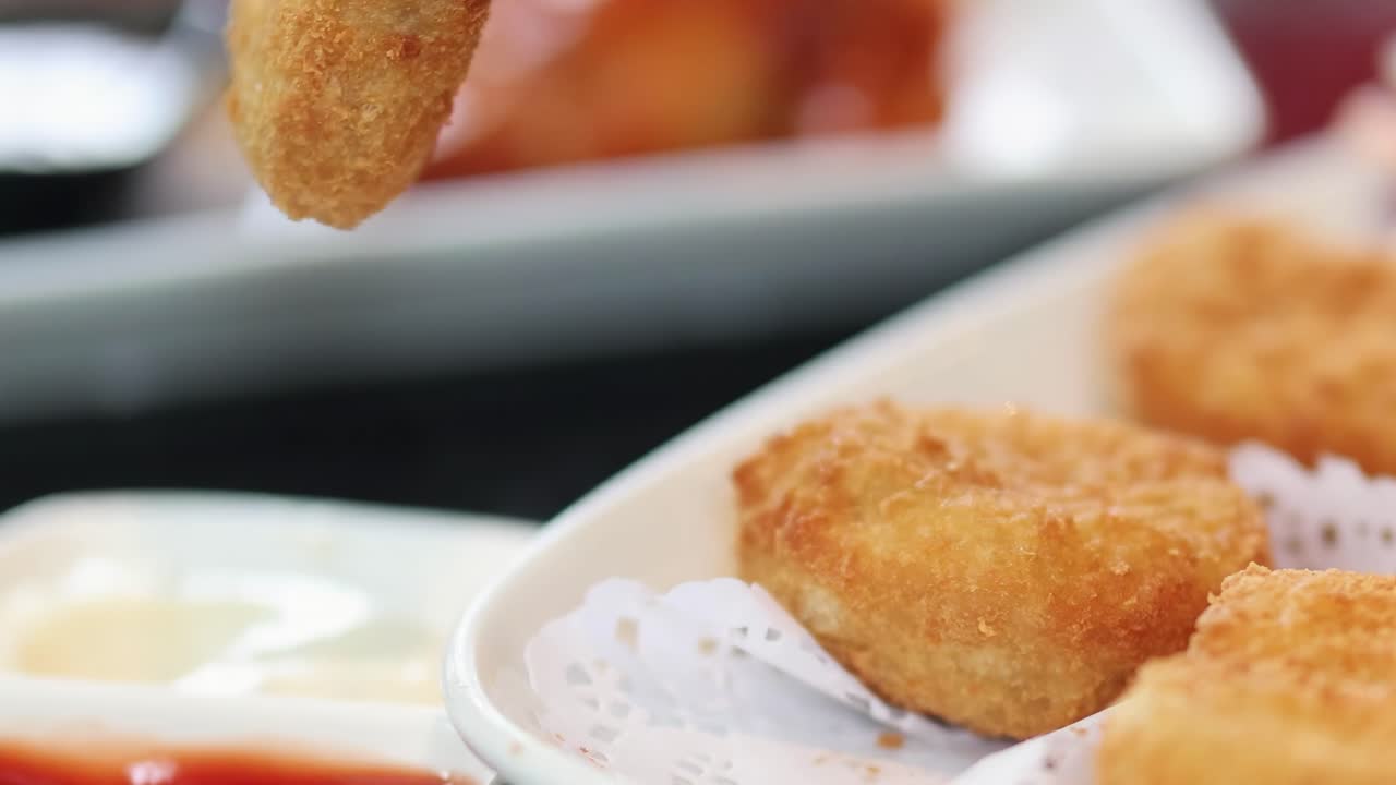 Close-up of chicken nuggets being dipped into ketchup and mayonnaise on a white plate.