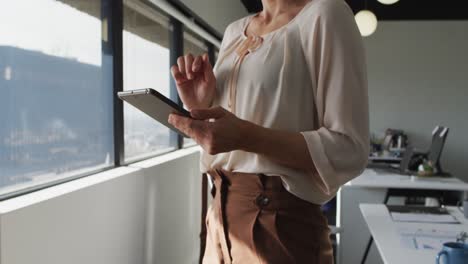 midsection of caucasian businesswoman standing and using tablet