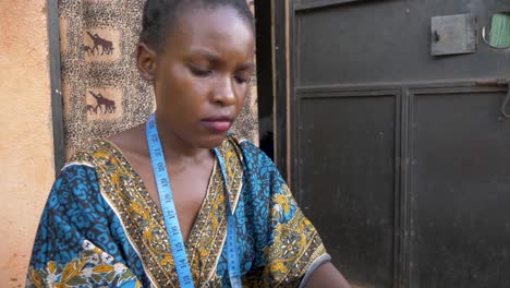 Close-up-slow-motion-shot-of-an-African-womans-face-as-she-sews-clothing-outside-her-home