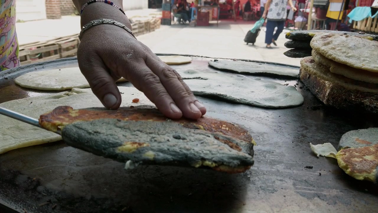 Primo piano di quesadillas tradizionali che cuociono su una grande piastra piatta in un vivace mercato di strada, mostrando l'autentica cucina messicana preparata al momento da un venditore locale