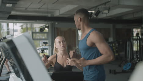 Caucasian-female-monitor-and-an-athletic-african-american-man-in-the-gym.