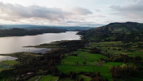 Drone zoom in shot revealing the Guatavita lake and green mountains under a cloudy sky in Colombia