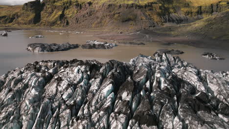 Aerial-reverse-dolly-from-pond,-flying-low-over-crevasses-on-glacier-surface