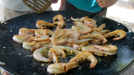 prawns and shrimps being cooked on an outdoor gas powered skottle pan and tossed in oil