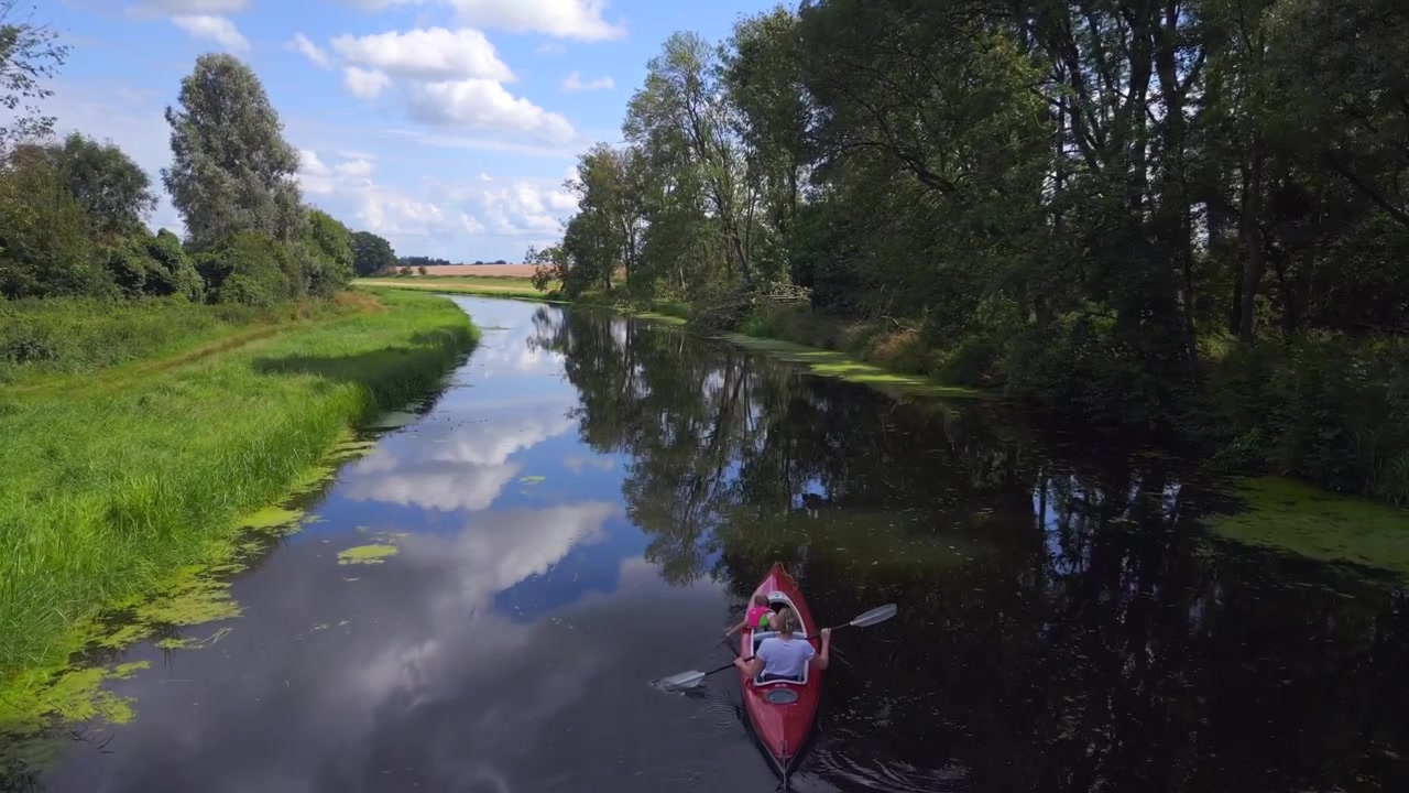 Perfekt flygbild uppifrån av en familjesemester med mamma och barn i en röd trampbåt på en naturflod, sommaren 2023 i Tyskland. Överflygning med drönare, 4K cinematiskt.