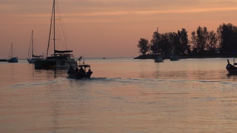 Tropische-Sonnenuntergangslandschaft,-Die-Die-Schimmernde-Himmelsreflexion-Auf-Der-Ruhigen-Wasseroberfläche-Einfängt,-Mit-Einem-Fischerboot,-Das-Vorwärts-Fährt,-Und-Einer-Luxuriösen-Yacht,-Die-In-Der-Bucht,-Der-Insel-Langkawi,-Malaysia,-Verankert-Ist