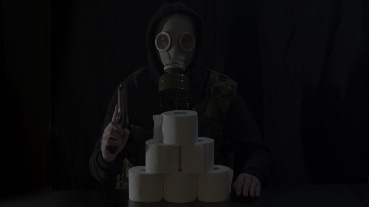 hombre con máscara de gas detrás de una pila de rollos de papel higiénico amartillando la pistola y apuntándola hacia la cámara
