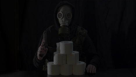 Gasmask-wearing-Man-behind-stack-of-toiletpaper-rolls-cocking-gun-and-aiming-it-towards-camera