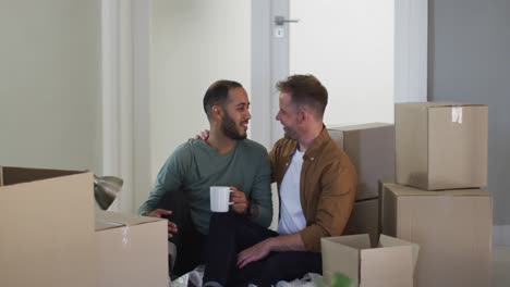 Multi-ethnic-gay-male-couple-drinking-coffee-and-packing-to-move-house