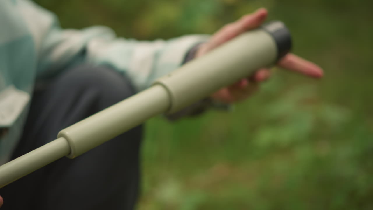 Mochileiro branco com mochila e garrafa térmica, usando gorro, monta um monóculo compacto e examina o topo das árvores com um olhar curioso sob a luz da floresta musgosa, exploração calma, momentos de observação e escotismo