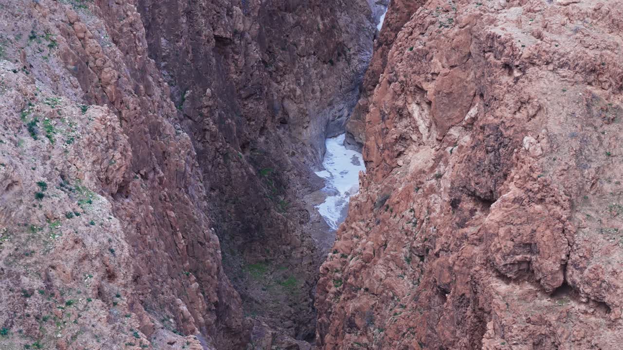 Vista aerea dall'alto con angolazione elevata che guarda in basso verso una gola profonda e stretta con ripide pareti di roccia rossa e un piccolo ruscello che scorre sul fondo