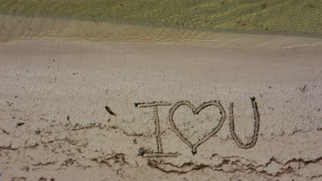 i heart u written in the sand and shifts to a slight angle as water laps onto the beach