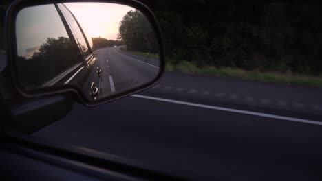 el sol poniente, visto en el espejo lateral de un camión en movimiento, en una carretera vacía en un entorno rural