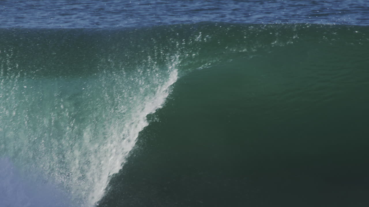 서핑 선수가 물에 떨어지는 동안 서서히 움직이는 바다 파도가 부히고, 생동감 넘치는 색상과 부드러운 황금색 조명이 물에서 반사됩니다.