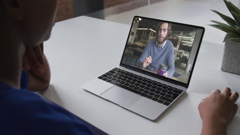 mujer de negocios afroamericana sentada en un escritorio usando una computadora portátil haciendo una videollamada con un colega masculino