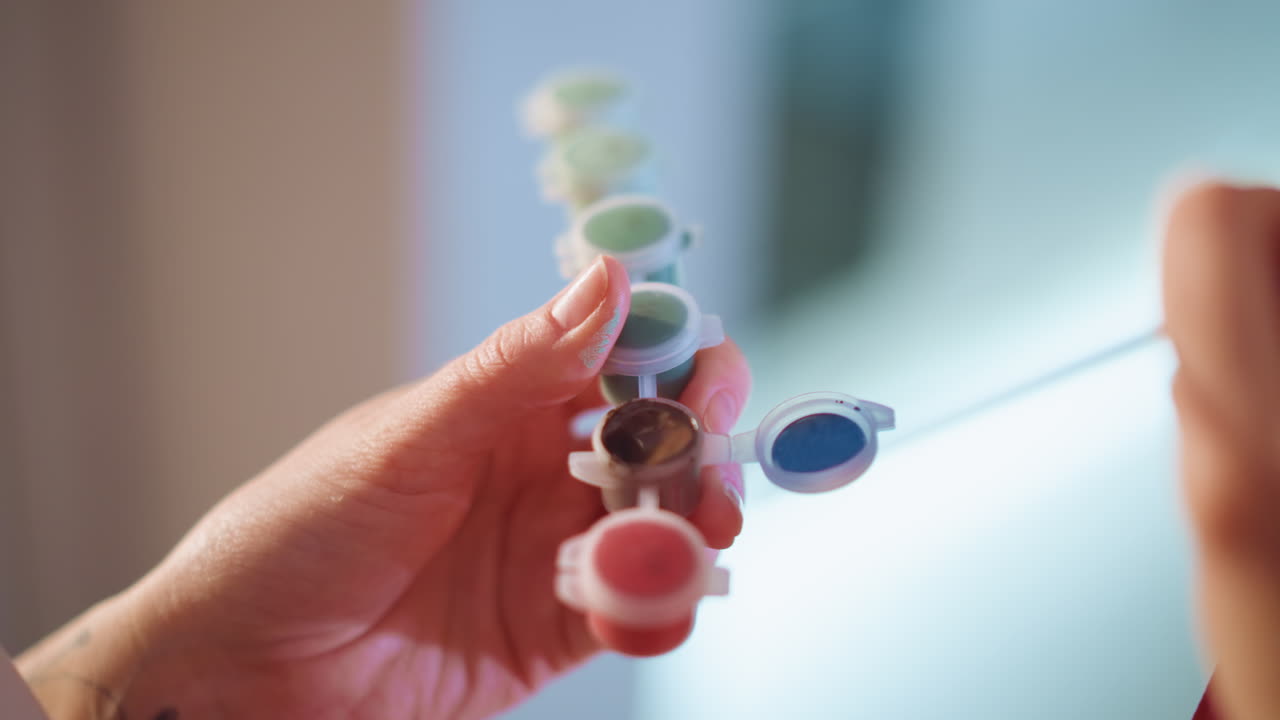 Close View Of Paint Palette Selection Process, Detailed Shot Of Hand Selecting Paint Under Soft Lighting, Intimate Depiction Of Fingers Delicately Choosing Shades From Small Pots Of Paint