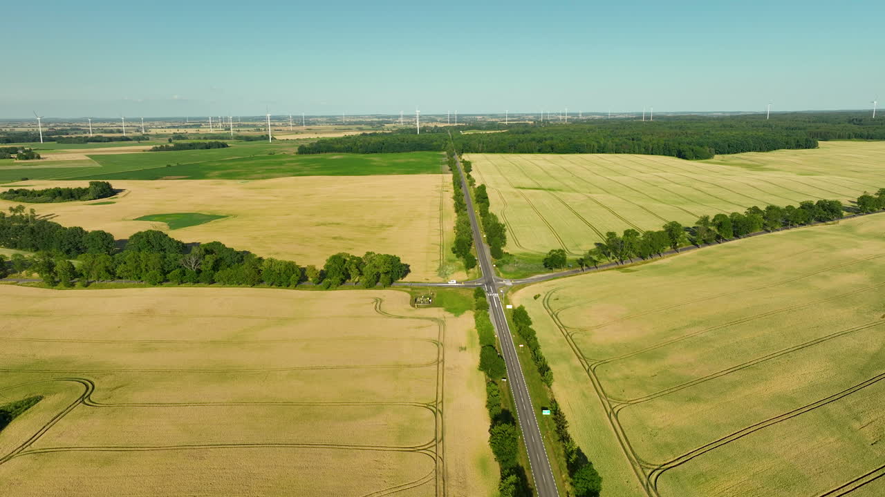 Aerial view of agricultural fields with a road and distant wind turbines