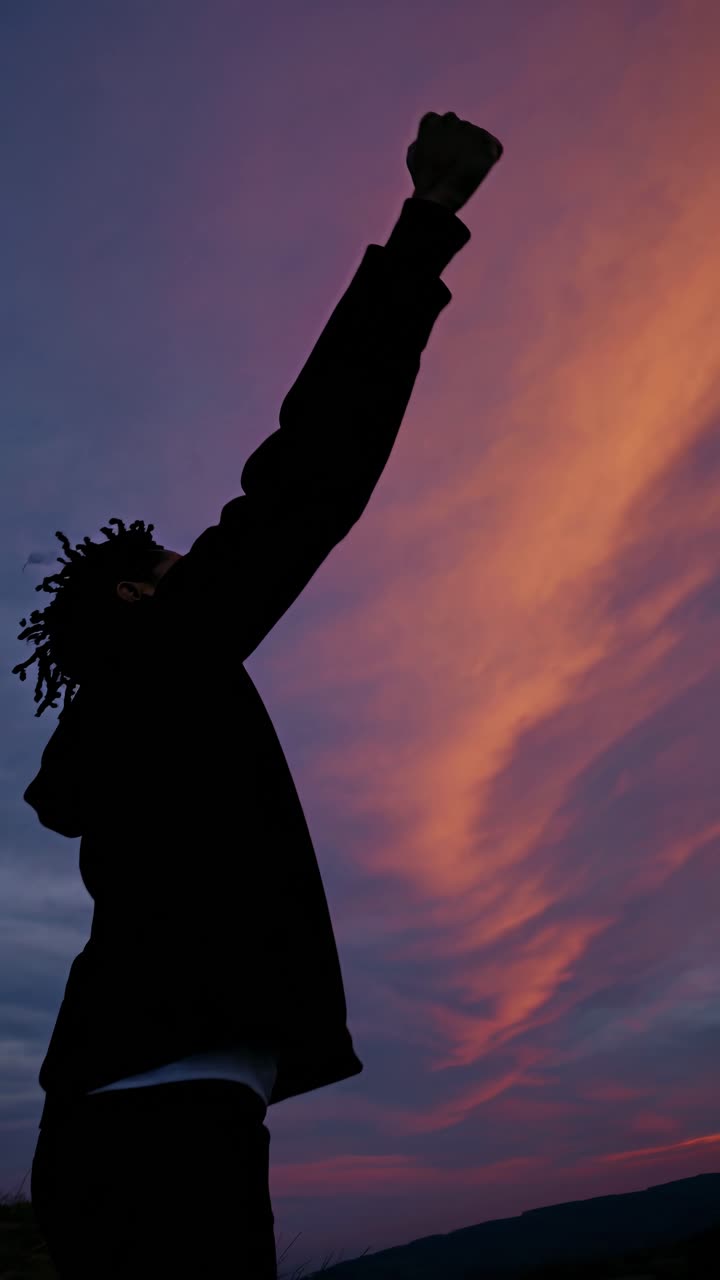 Silhouette d'une personne le poing levé sur fond de ciel de coucher de soleil éclatant
