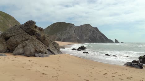 las frías olas del océano atlántico se estrellan en la playa cerca de la montaña gruta da adraga