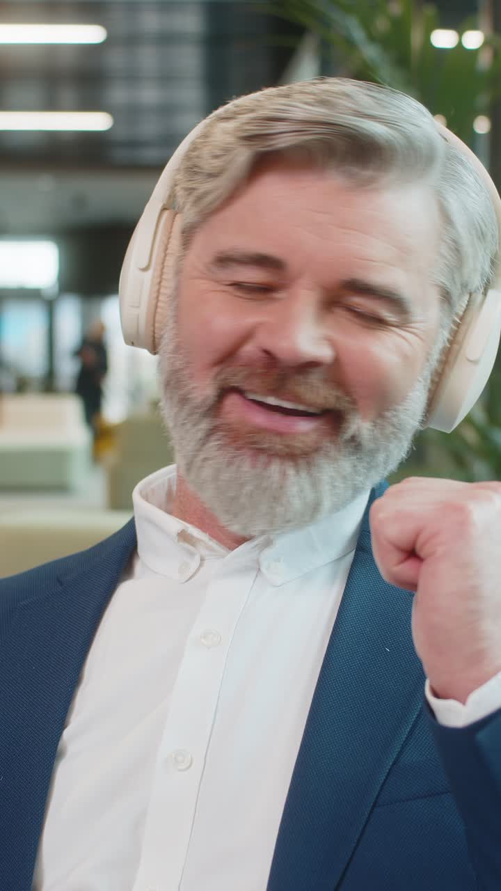 hombre de negocios relajado de mediana edad con auriculares escuchando música en su teléfono inteligente en el vestíbulo de una oficina moderna