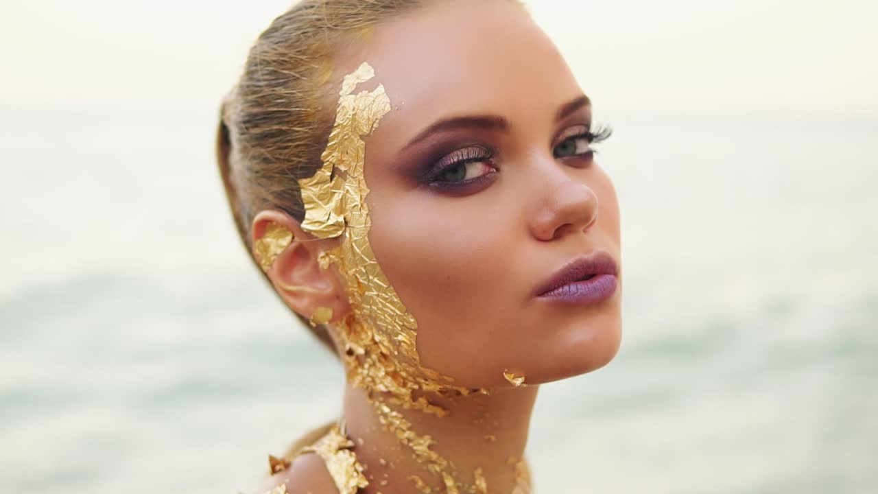A sexy woman with professional golden makeup looks at the camera and flirts with the viewer. Attractive model standing by the