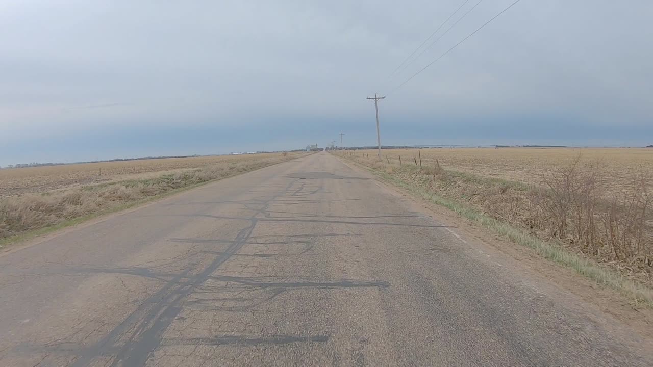 흐린 겨울날 네브래스카 중남부의 수확된 들판 사이의 오래된 아스팔트 도로에서 운전하는 동안 뒷창 보기