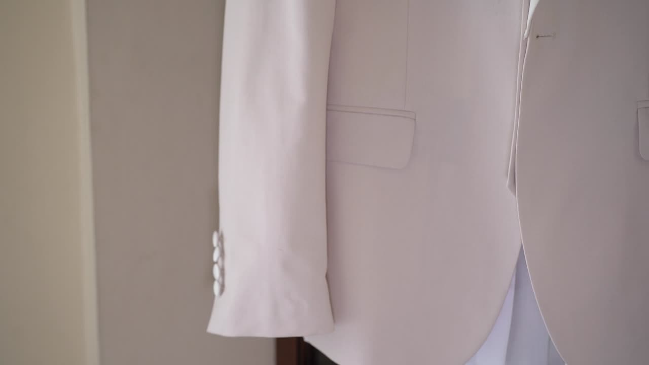 Un blazer bianco è appeso in esposizione in un camerino. L'attenzione è focalizzata sul suo design e sulla luce che entra dalla finestra vicina mentre qualcuno si prepara per una prova.