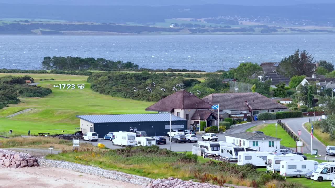 Wide shot of golf course, caravan park, and seaside landscape under bright daylight, slight pan