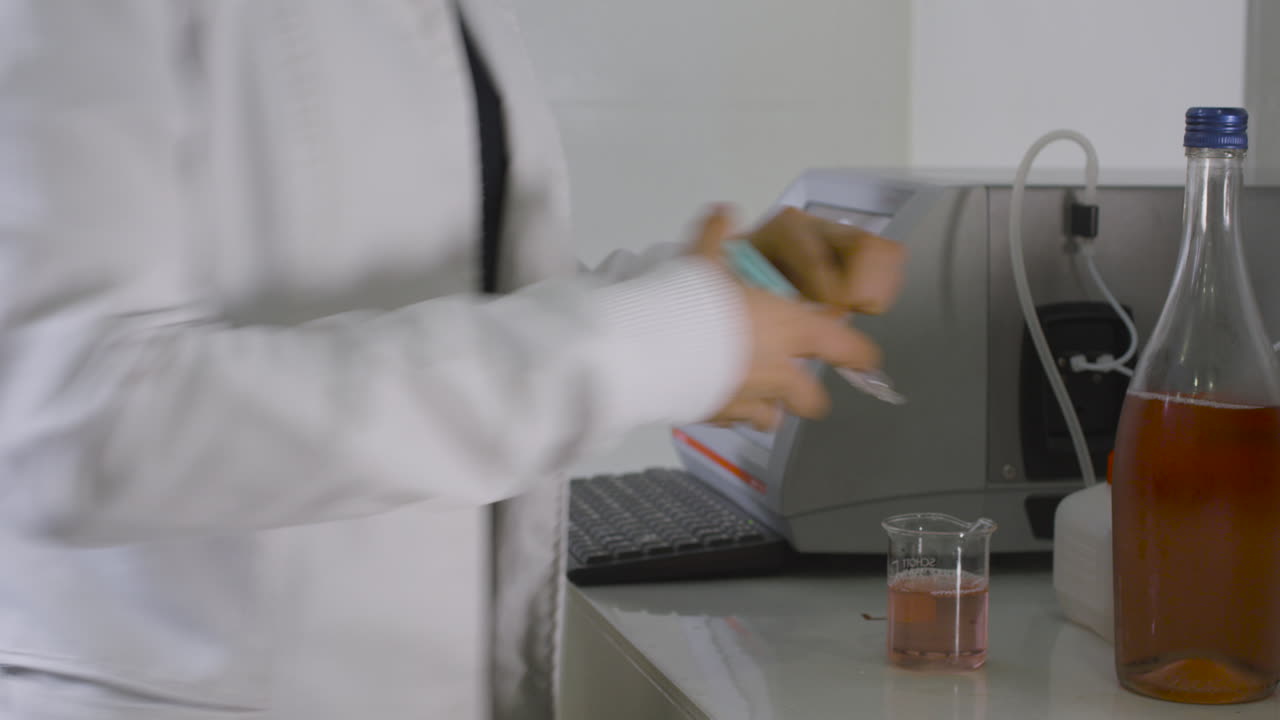Medium shot of a scientist in a white coat pouring a wine sample into a beaker in a laboratory setting. An ideal clip for depicting wine quality analysis.