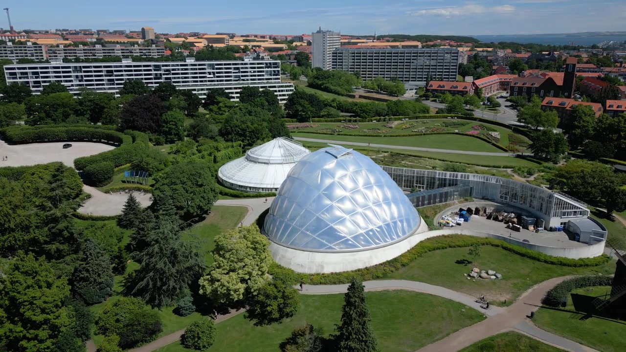 Casas Tropicais no Jardim Botânico de Aarhus com cúpulas de vidro em meio a um parque verdejante, vista aérea em órbita para a esquerda