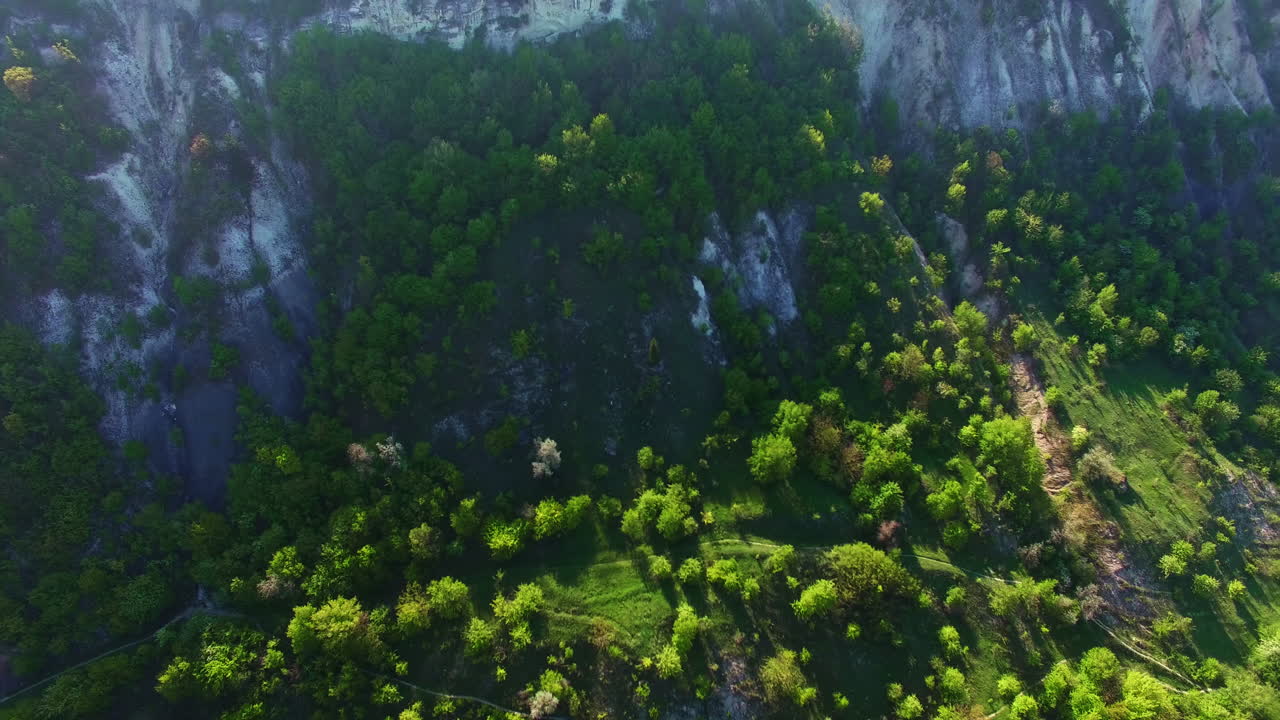 Sloping mountains with trees growing on. White rock covered with vegetation in the rays of sun. Top view.