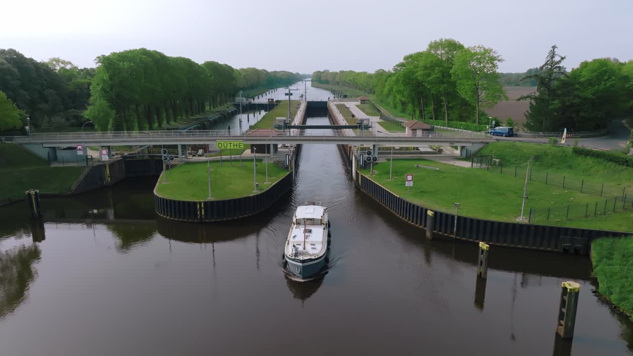 Aerial zoom out from a barge leaving Doerpen Lock on the Küstenkanal, showing symmetrical canal design and surrounding greenery under clear skies.
